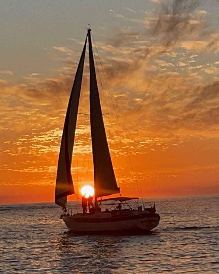 El Key Breeze a toda vela con el sol poniéndose entre sus velas